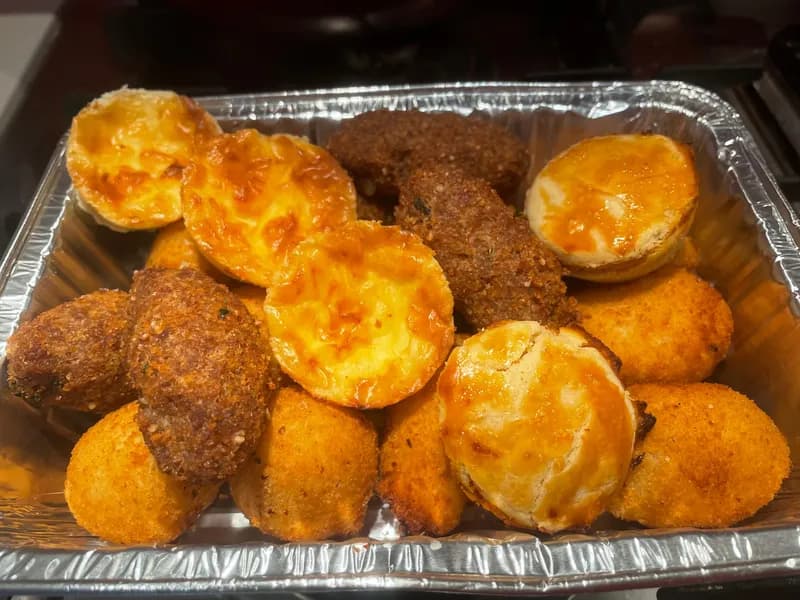 A foil tray packed with empadinhas, quibes and coxinhas, ready to go