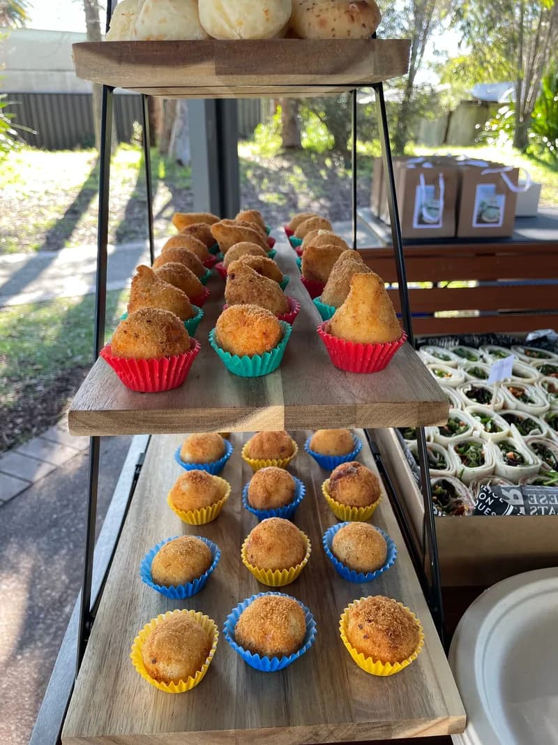 Coxinhas and bolinhas de queijo in coloured paper cases on a two-tier wooden stand, in a garden